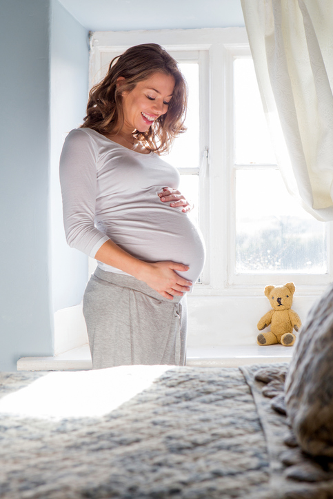 Pregnant woman looking down at her belly with a smile on her face.
